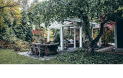 Outdoor patio area with a wooden table and chairs under a pergola in a garden setting.