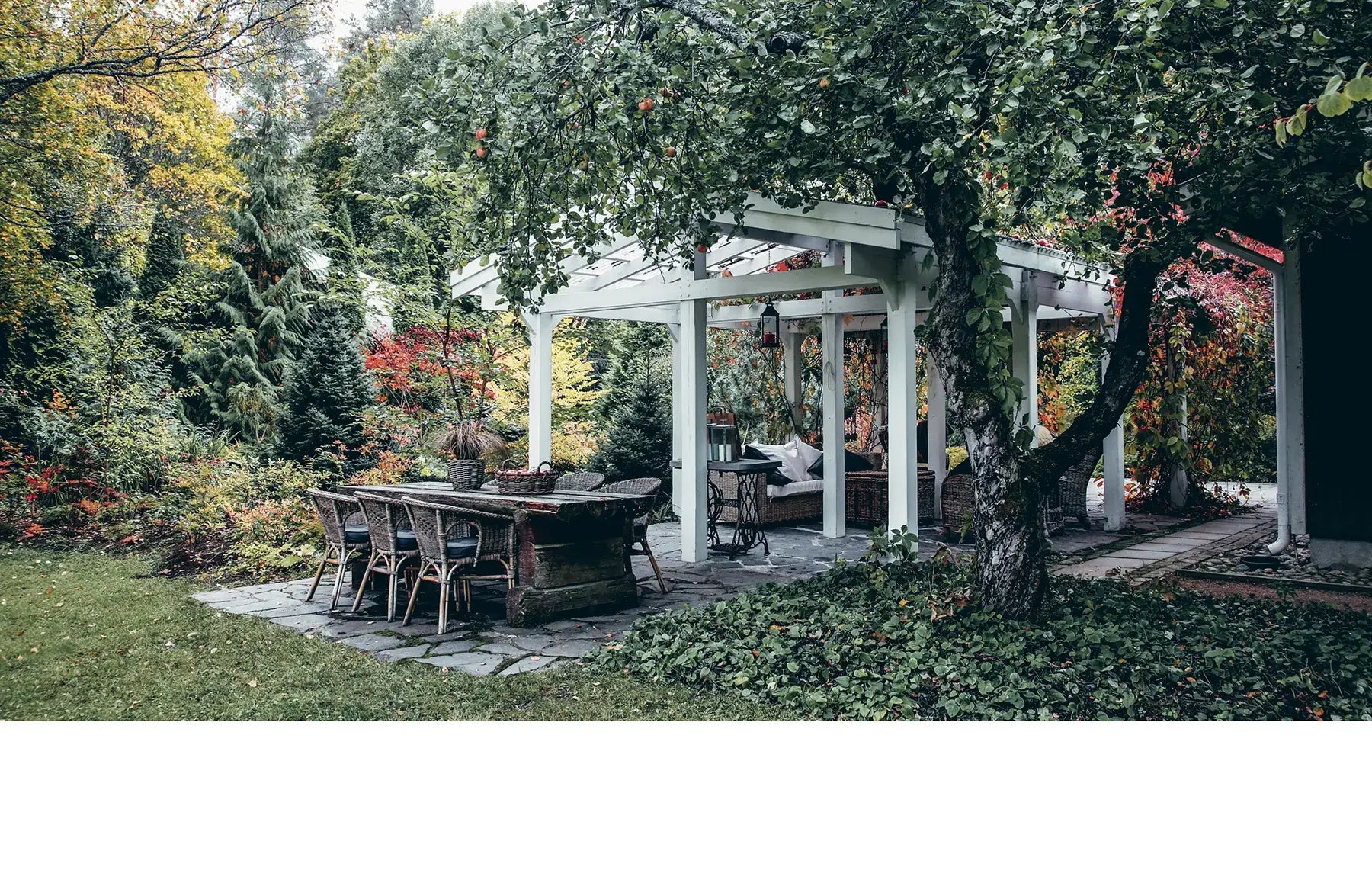 Outdoor patio area with a wooden table and chairs under a pergola in a garden setting.