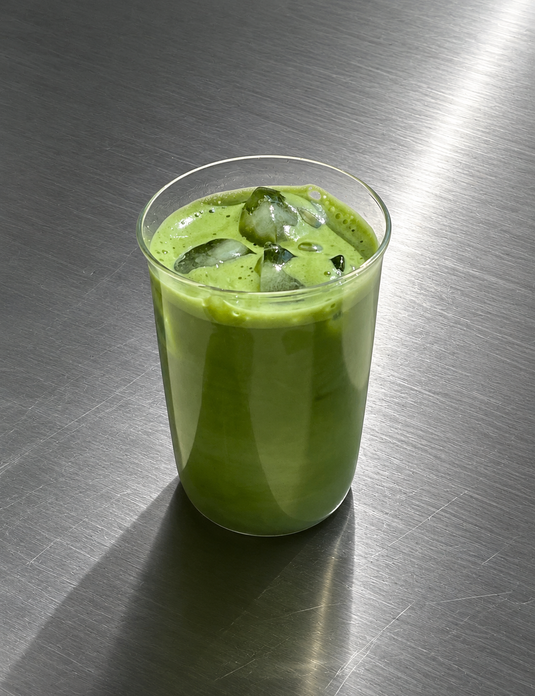 Green iced matcha drink in a glass on a metallic surface